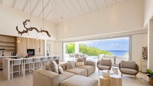 Uma sala de estar moderna com um amplo sofá em formato de L, cozinha e vista para o oceano.