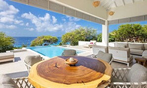 An outdoor seating area with a round wooden table, lounge chairs, and a view of the ocean. - Luxury seaside retreat with private beach (Sint Willibrordus)