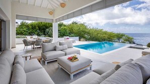 Uma área externa moderna com piscina, espaço para sentar e vista para o mar.