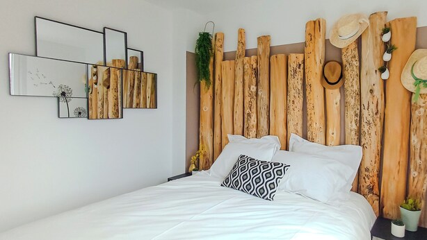 Un dormitorio con cabecera de madera, ropa de cama blanca y un espejo fijado a la pared.