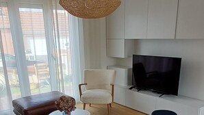 Una sala de estar moderna con un televisor de pantalla plana, una lámpara colgante de mimbre y un ventanal con vistas al exterior.
