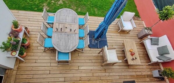 Une terrasse en bois avec une table et des chaises au centre, entourée de plantes en pot et de mobilier d’extérieur.