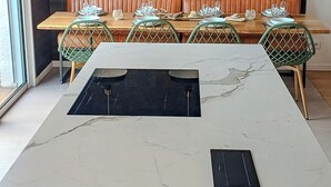 Una cocina moderna con encimera de mármol blanco, grifo de cobre y placa de inducción negra.