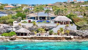 A coastal property with a stone retaining wall, a pool, and a house with a solar panel roof. - Elegant seaside retreat with private beach - Coral Estate (Sint Willibrordus)