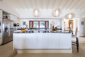 A modern kitchen with a large island, stainless steel appliances, pendant lighting, and a view to the outdoors. - Elegant seaside retreat with private beach (Sint Willibrordus)