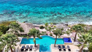 An aerial view of a resort with a large swimming pool, palm trees, and a beach. - Elegant seaside retreat with private beach - Coral Estate (Sint Willibrordus)