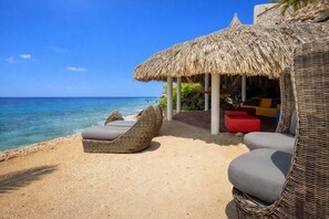 A beachside lounge with wicker furniture, a thatched roof, and a view of the ocean. - Elegant seaside retreat with private beach (Sint Willibrordus)