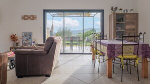 Una sala de estar con un sofá, una mesa de comedor con sillas, un aparador y vistas a través de un ventanal.