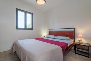 Een slaapkamer met een bed, nachtkastje, lamp en raam.
