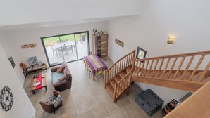 Amplia sala de estar con escalera de madera, una mesa de comedor con sillas y vistas al exterior.