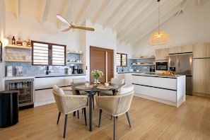 A modern kitchen with a dining area, featuring a central island, built-in appliances, and a ceiling fan. - Spacious luxury villa with panoramic sea views (Sint Willibrordus)