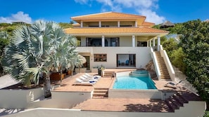 Une maison à deux étages avec une piscine, un escalier menant à l’étage supérieur et un grand arbre au premier plan.