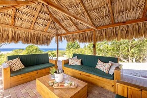 Un espacio al aire libre techado con dos sofás verdes y una mesa de centro de madera, con vistas a un paisaje pintoresco.
