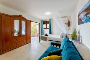 Ein Zimmer mit einem Holzschrank, einem blauen Sofa, einem Bett mit weißem Baldachin und Blick auf Grünlandschaft.