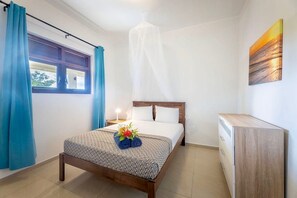 Ein Hotelzimmer mit einem Bett, einem Nachttisch mit Lampe, einem Fenster mit Vorhängen und einem Bild an der Wand.