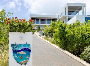 A pathway leading to a modern building with a signboard displaying a coastal scene and the number 537. - Design villa with sea views and infinity pool (Sint Willibrordus)