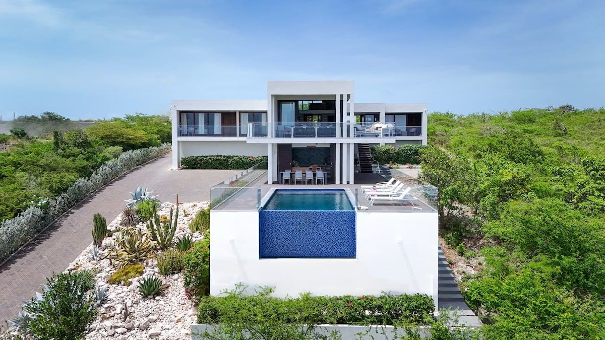 A modern two-story house with a swimming pool, surrounded by greenery.