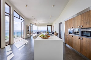 Cozinha moderna com ilha central, grandes janelas e vista para o oceano.