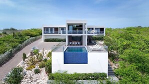 Una casa moderna de dos pisos con piscina, rodeada de exuberante vegetación.