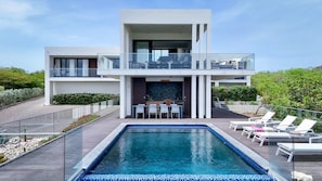 Uma casa moderna de dois andares com piscina, área de estar externa e varanda.