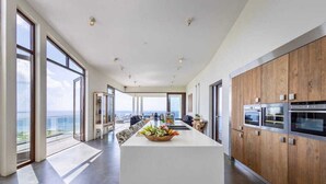 Una cocina moderna con una isla central, armarios de madera y ventanas amplias con vistas al mar.