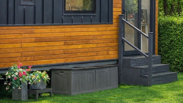 A modern building with a combination of dark siding and wooden accents, featuring multiple windows and a door with a small set of stairs leading up to it. - Old Mill Tiny Homes (Yarm)