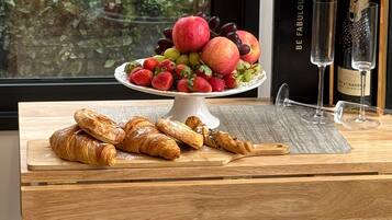 A wooden table with a fruit platter, two glasses, and a bottle of champagne.