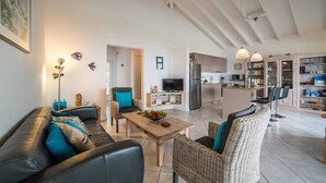 Ein modernes Wohnzimmer mit einer Couch, Sesseln, einem Couchtisch und einer Küche im Hintergrund.