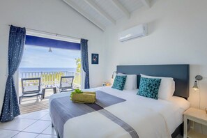 A hotel room with a bed, a nightstand, a lamp, a window with curtains, and a view of the sea. - Panoramic sea-view villa with private pool (Sint Willibrordus)