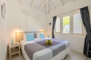 A hotel room with a bed, bedside tables, a window with curtains, and an air conditioning unit.
