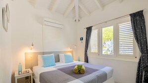 Ein aufgeräumtes Schlafzimmer mit einem Bett, Nachttischen, einem Fenster mit Vorhängen und einer Wand-Klimaanlage.