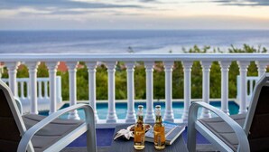 Ein Tisch am Pool mit zwei Bierflaschen und einer Speisekarte, mit Blick auf ein Schwimmbecken mit weißer Brüstung und den Blick auf den Ozean.