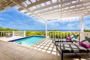 Ein überdachter Außenbereich mit Pool, Liegestühlen und Blick aufs Meer.