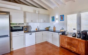 A modern kitchen with white cabinetry, a built-in oven, a dishwasher, and a wooden countertop with a coffee maker. - Spacious villa with pool and ocean views (Sint Willibrordus)