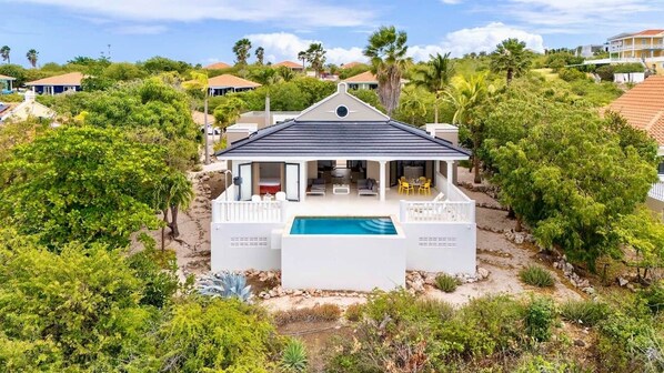 A white house with a pool, surrounded by greenery and other houses in the background. - Designer sea-view villa with private pool - Coral Estate (Sint Willibrordus)
