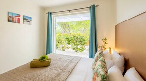 A hotel room with a bed, a small table with a plant, a view of greenery outside, and artwork on the wall. - Modern villa with private pool and garden views (Sint Willibrordus)