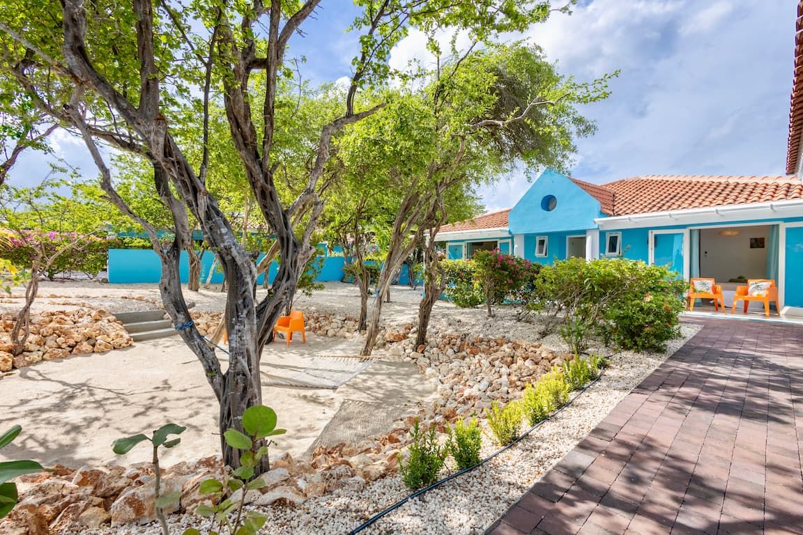 Um edifício azul com telhado em cerâmica, rodeado por árvores e um caminho de cascalho.
