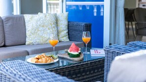 Morgenmad med croissanter, vandmelon og appelsinjuice på et bord i et rum med fletmøbler og en blå væg.
