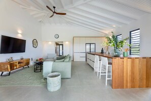 A spacious living area with a wooden bar, a sofa, a television, and a ceiling fan. - Modern villa with infinity pool and sea views (Sint Willibrordus)