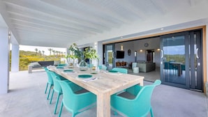 A spacious outdoor dining area with a wooden table and turquoise chairs, overlooking a scenic landscape. - Modern villa with infinity pool and sea views - Coral Estate (Sint Willibrordus)