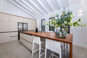 A modern kitchen with a wooden countertop, white chairs, and a large vase of flowers. - Modern villa with infinity pool and sea views (Sint Willibrordus)