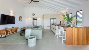 A spacious living area with a wooden bar, a sofa, a television, and a ceiling fan. - Modern villa with infinity pool and sea views - Coral Estate (Sint Willibrordus)