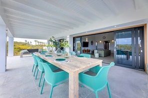 A spacious outdoor dining area with a wooden table and turquoise chairs, overlooking a scenic landscape. - Modern villa with infinity pool and sea views (Sint Willibrordus)