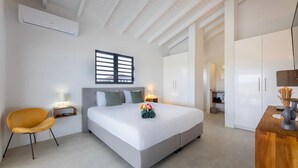 A modern hotel room with a large bed, a wooden side table, a chair, a wardrobe, and a window with blinds. - Modern villa with infinity pool and sea views - Coral Estate (Sint Willibrordus)