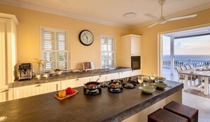 A kitchen with a large island, a clock, and a view of the ocean. - Serene luxury retreat with pool and sea views (Sint Willibrordus)