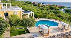 A residential property with a swimming pool, outdoor seating, and a view of the ocean. - Serene luxury retreat with pool and sea views (Sint Willibrordus)