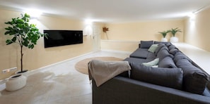 A living room with a sectional sofa, a flat-screen TV mounted on the wall, a potted plant, and a large window. - Serene luxury retreat with pool and sea views (Sint Willibrordus)