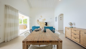 A dining area with a wooden table, chairs, a vase with flowers, a blue sofa, and a wooden cabinet. - Sea-view villa with private magnesium pool - Coral Estate (Sint Willibrordus)
