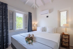 Ein Hotelzimmer mit einem Bett, zwei Nachttischen, einem Fenster mit Rollläden und einer Klimaanlage.