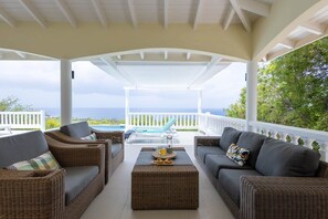 A covered outdoor seating area with wicker furniture and a view of the ocean.